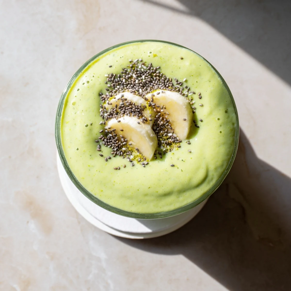 Vibrant green Greek yogurt avocado smoothie topped with chia seeds and sliced banana garnish