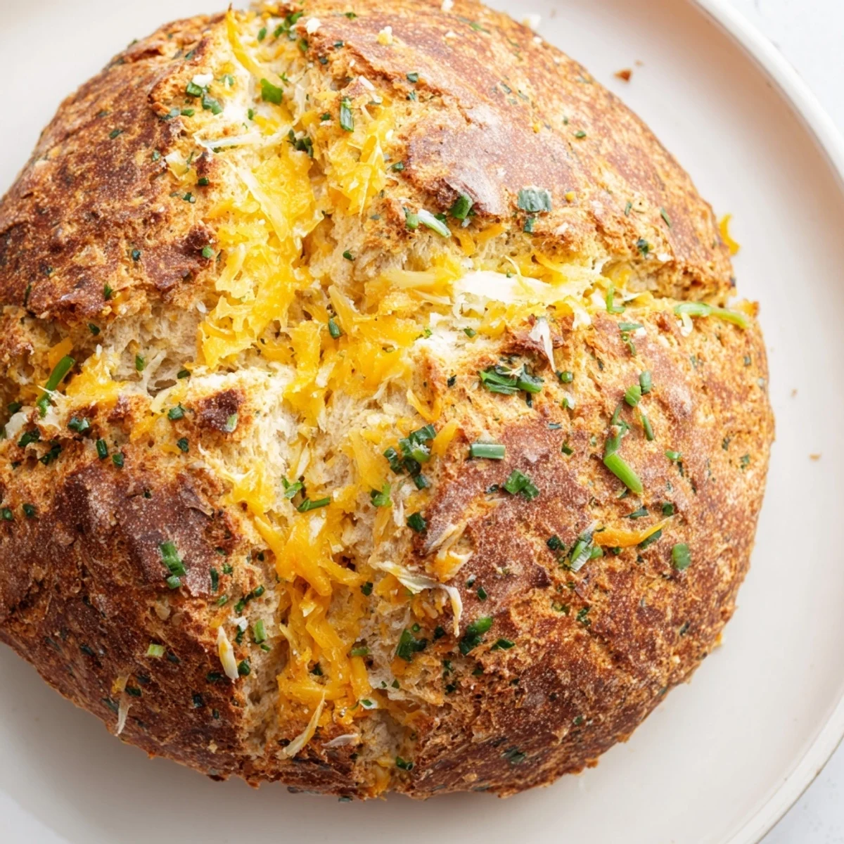 Golden cheddar and herb soda bread loaf with a cross-cut top and flecks of fresh green herbs throughout the crusty exterior