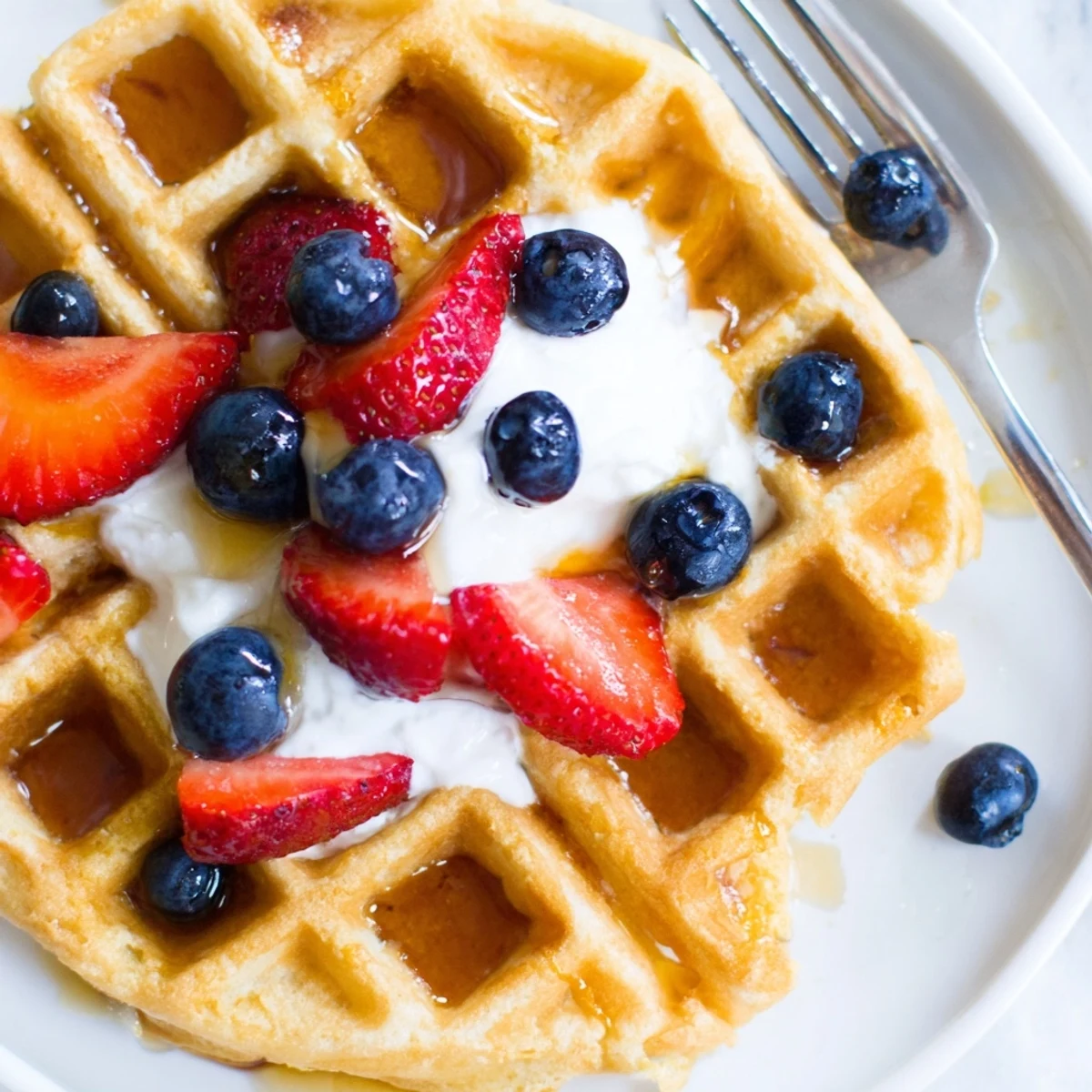 Golden Greek Yogurt Waffles topped with fresh berries and maple syrup on a white plate