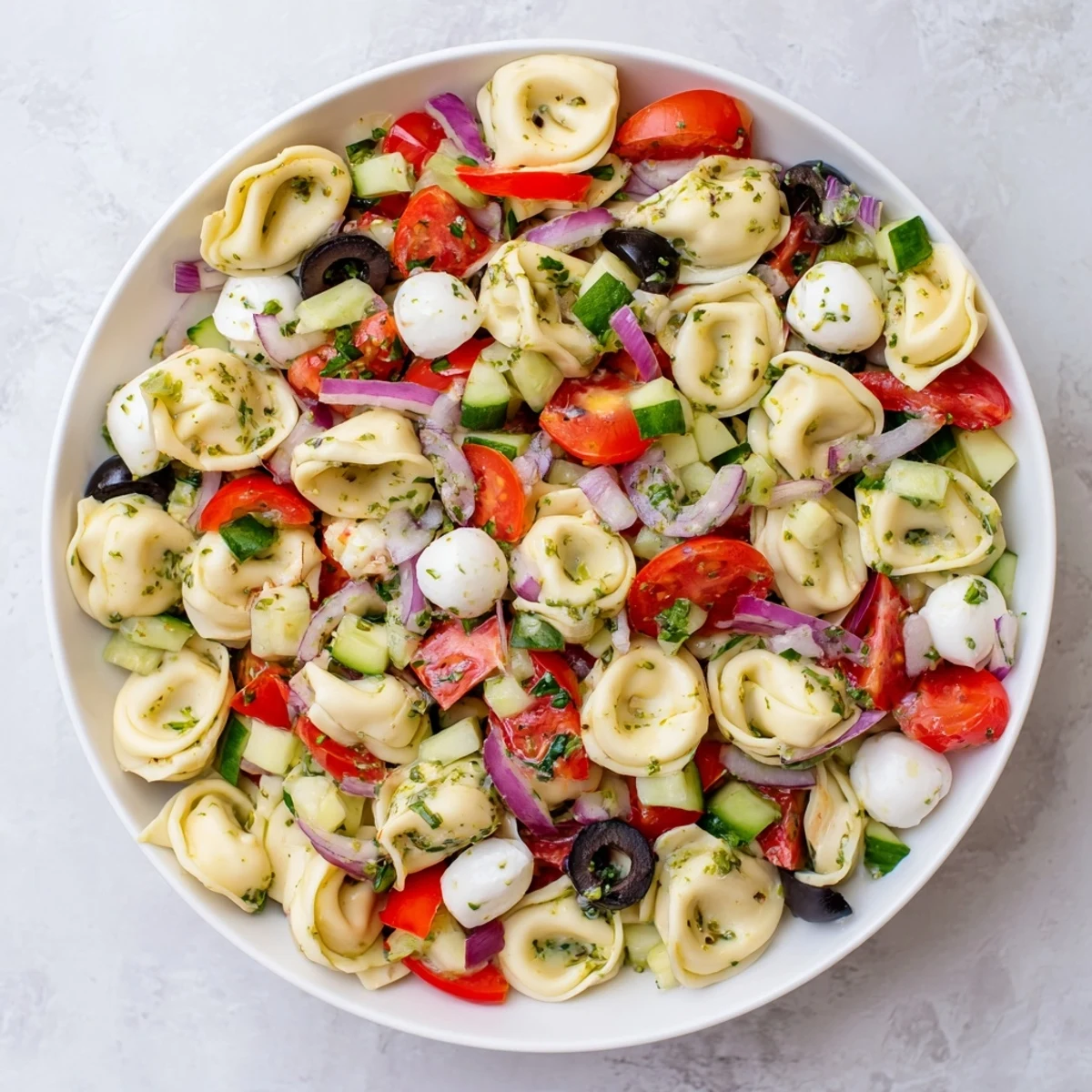 Tortellini Pasta Salad in a white bowl with colorful cherry tomatoes and cucumber chunks