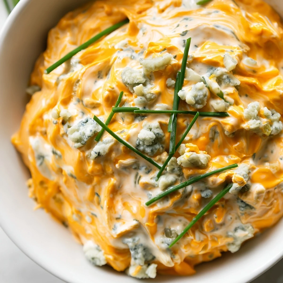 Creamy buffalo pickle dip in a serving bowl surrounded by crunchy chips and fresh veggie sticks for dipping