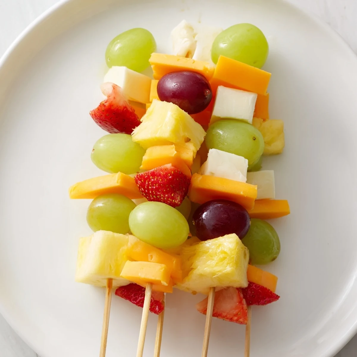 Colorful fruit and cheese kabobs arranged on platter with ripe grapes and cheddar cubes