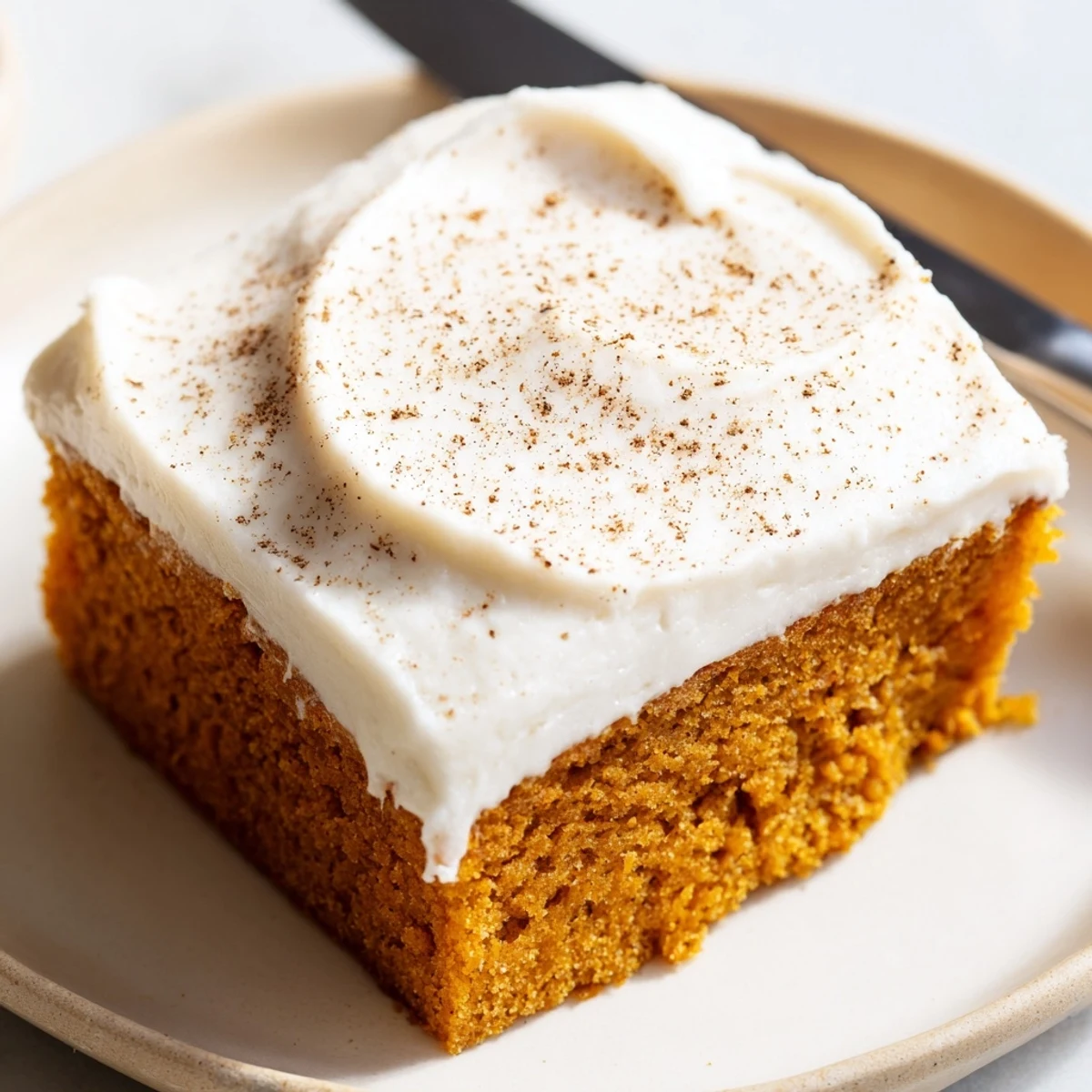 Warm spiced pumpkin bars with cream cheese frosting sliced and plated on rustic parchment paper