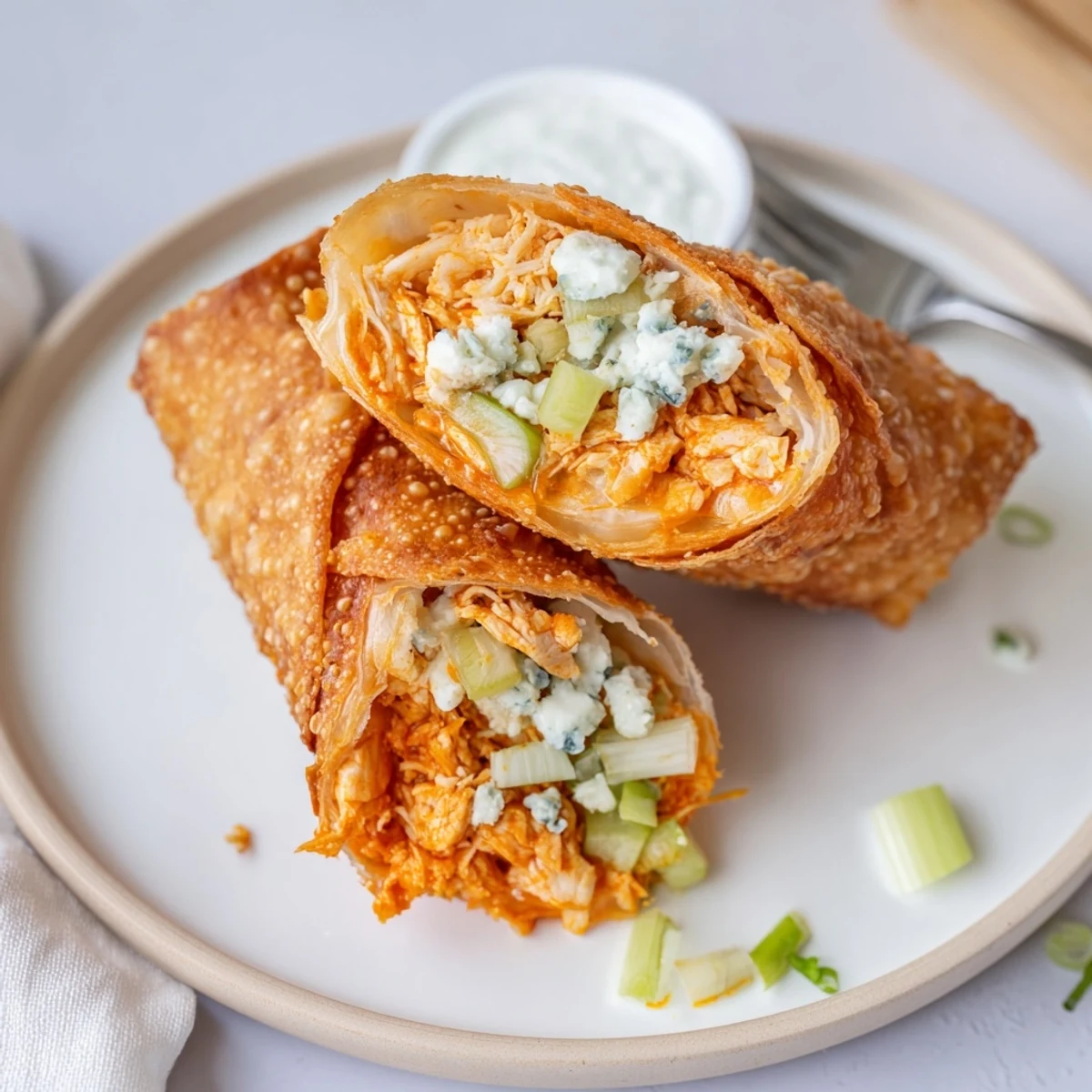 Crispy Buffalo Chicken Egg Rolls oozing cheesy filling beside ranch dipping sauce.