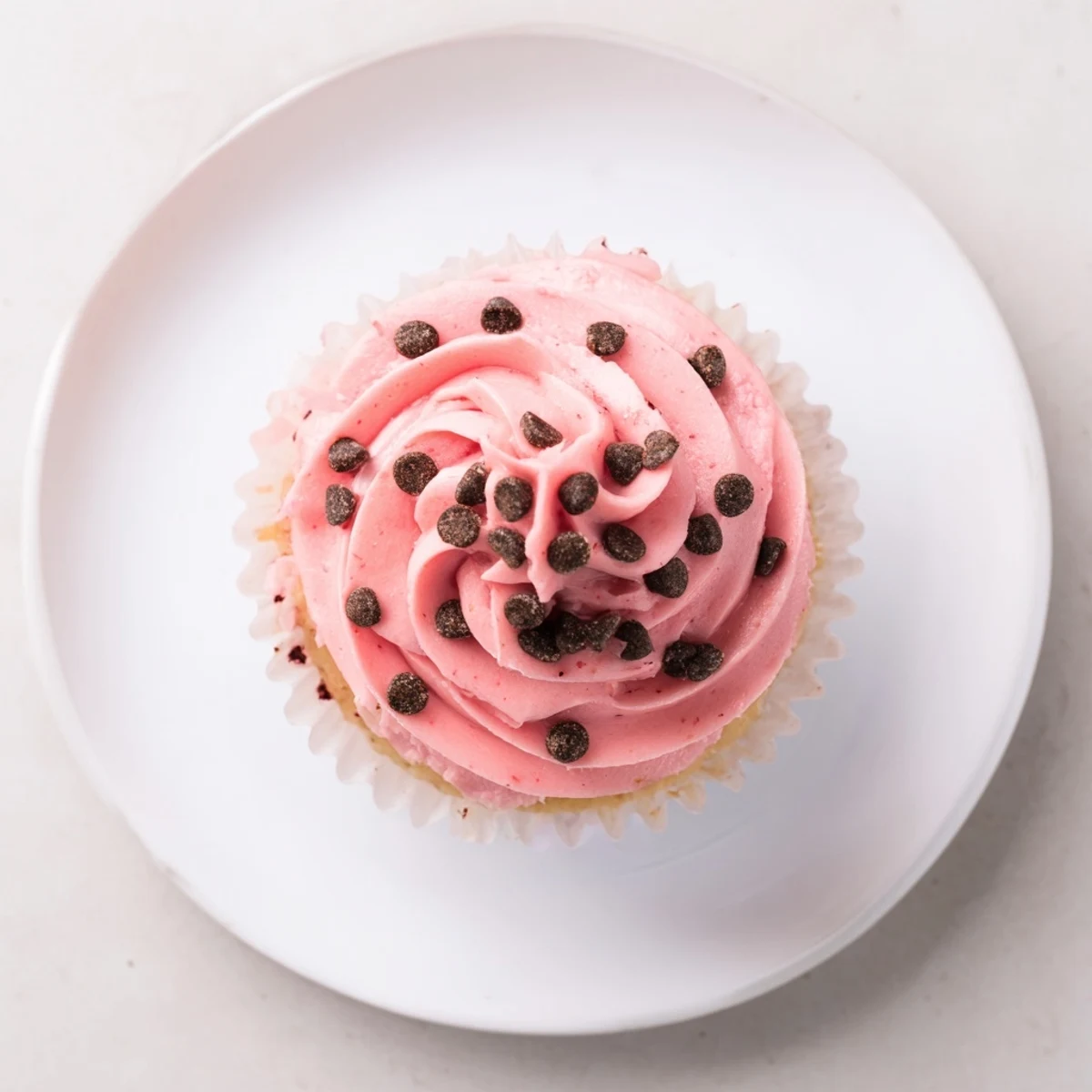 Moist watermelon cupcakes topped with creamy pink frosting and mini chocolate chip seeds on a white plate