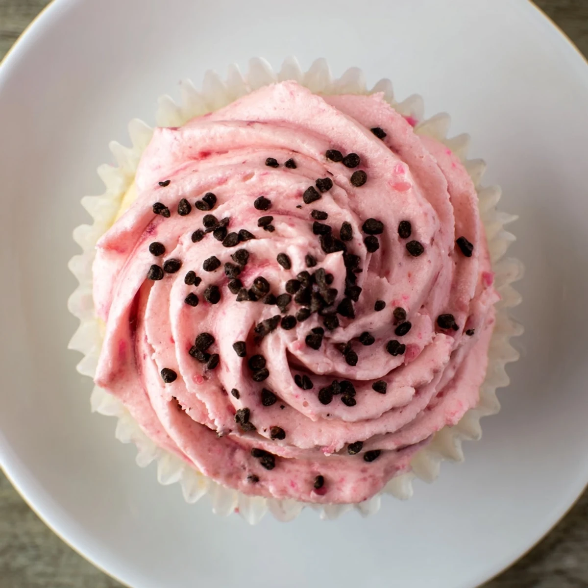 Freshly baked watermelon cupcakes with swirls of watermelon buttercream frosting and seed detailing on a wire cooling rack