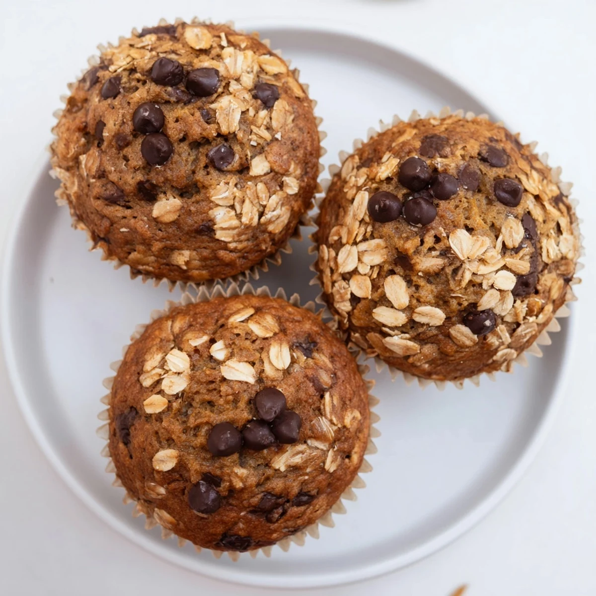 Freshly baked banana chocolate chip muffins with oats, topped with melting chocolate chips on a rustic wooden board