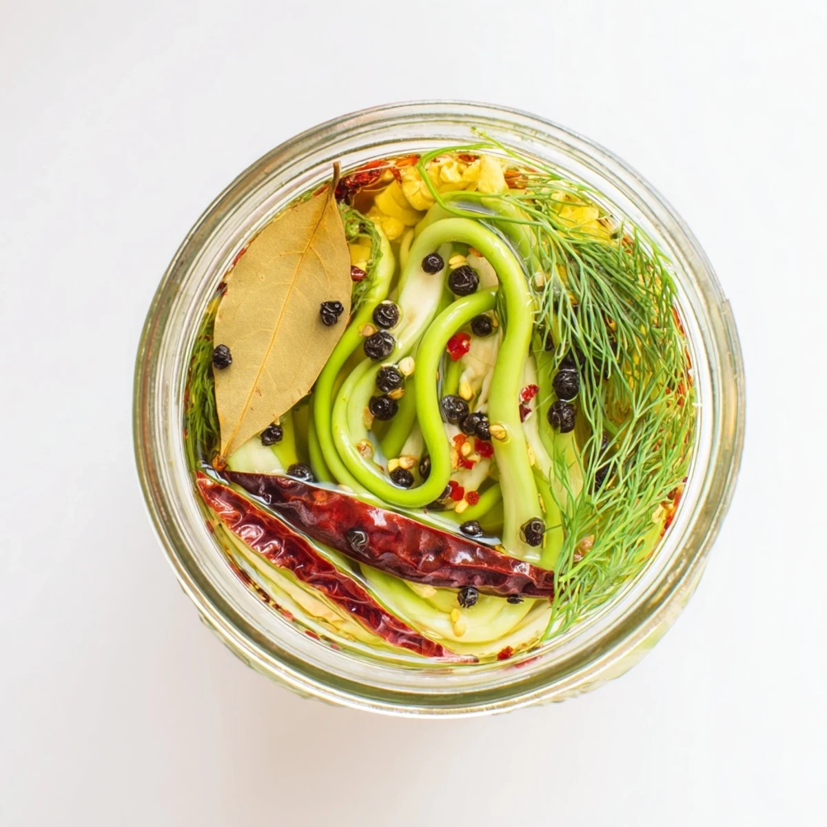 Spicy pickled garlic scapes packed in mason jars with red chili flakes and dill sprigs