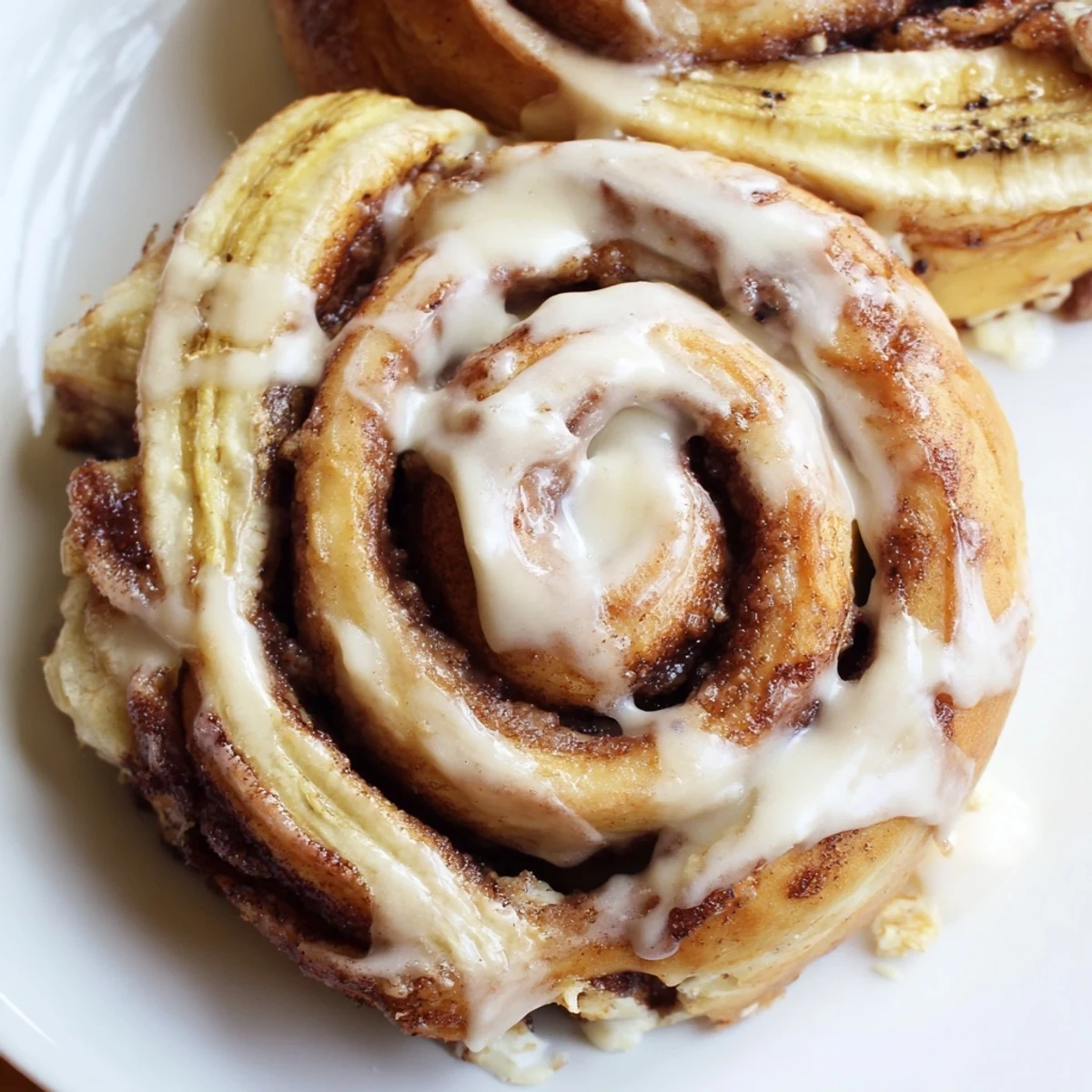 Freshly baked banana cinnamon rolls drizzled with creamy white glaze on a wooden board