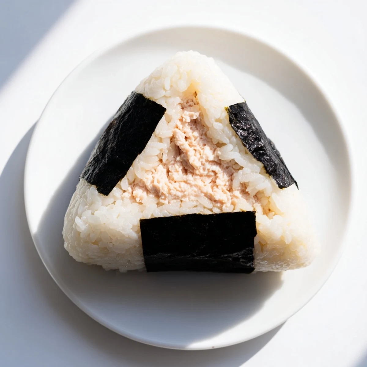 Handheld tuna mayo onigiri showcasing fluffy white rice with savory tuna center