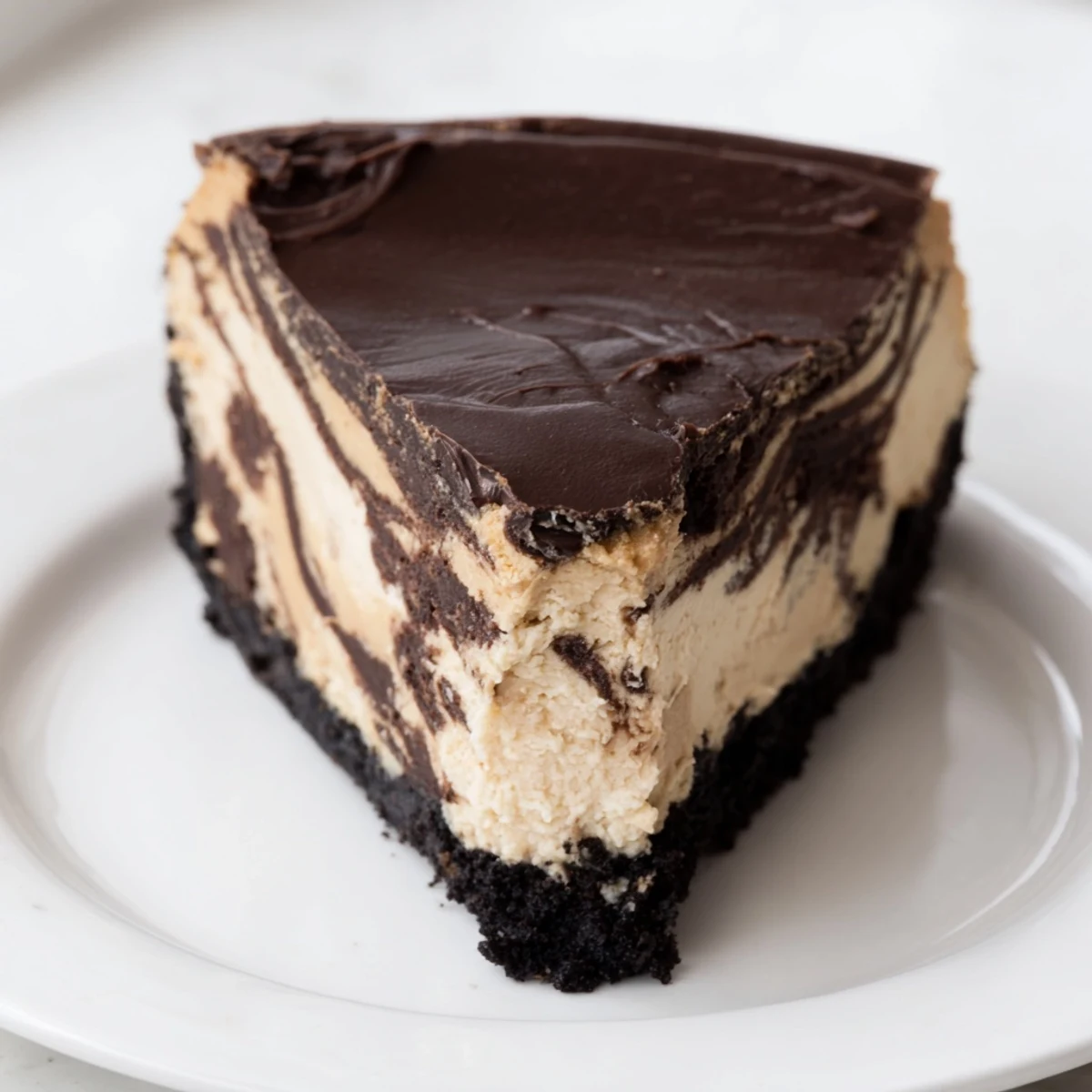 Silky chocolate peanut butter cheesecake topped with glossy ganache on a dessert plate