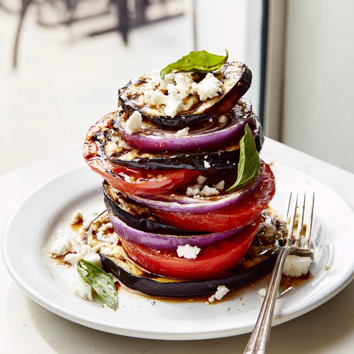 Smoky grilled tomato eggplant stacked on a platter with fresh basil and crumbled feta