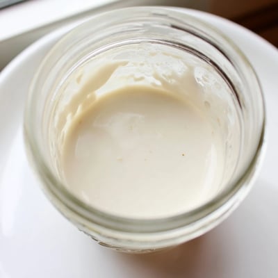 Creamy condensed coconut milk pooling in a small glass jar